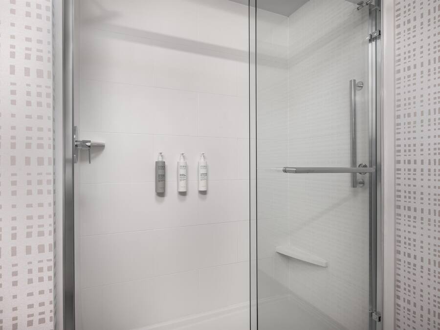 A modern bathroom with a glass shower enclosure, white tiled walls, and three toiletries on the wall.
