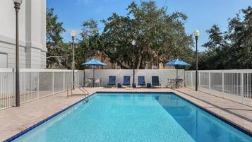 A swimming pool with blue tiles, white railings, and blue umbrellas.