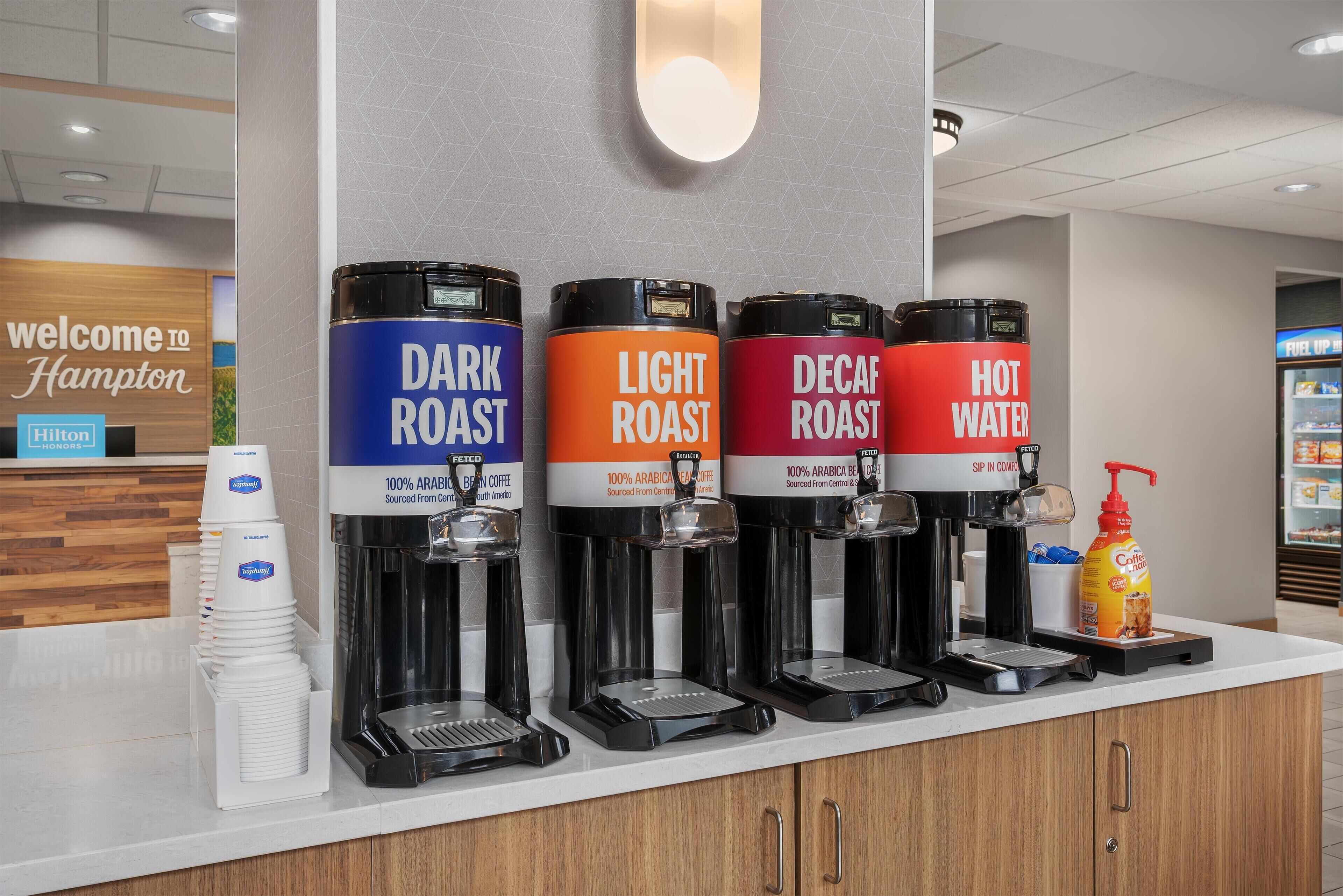 Una estación de café con cuatro dispensadores etiquetados como: tostado oscuro, tostado claro, descafeinado y agua caliente.