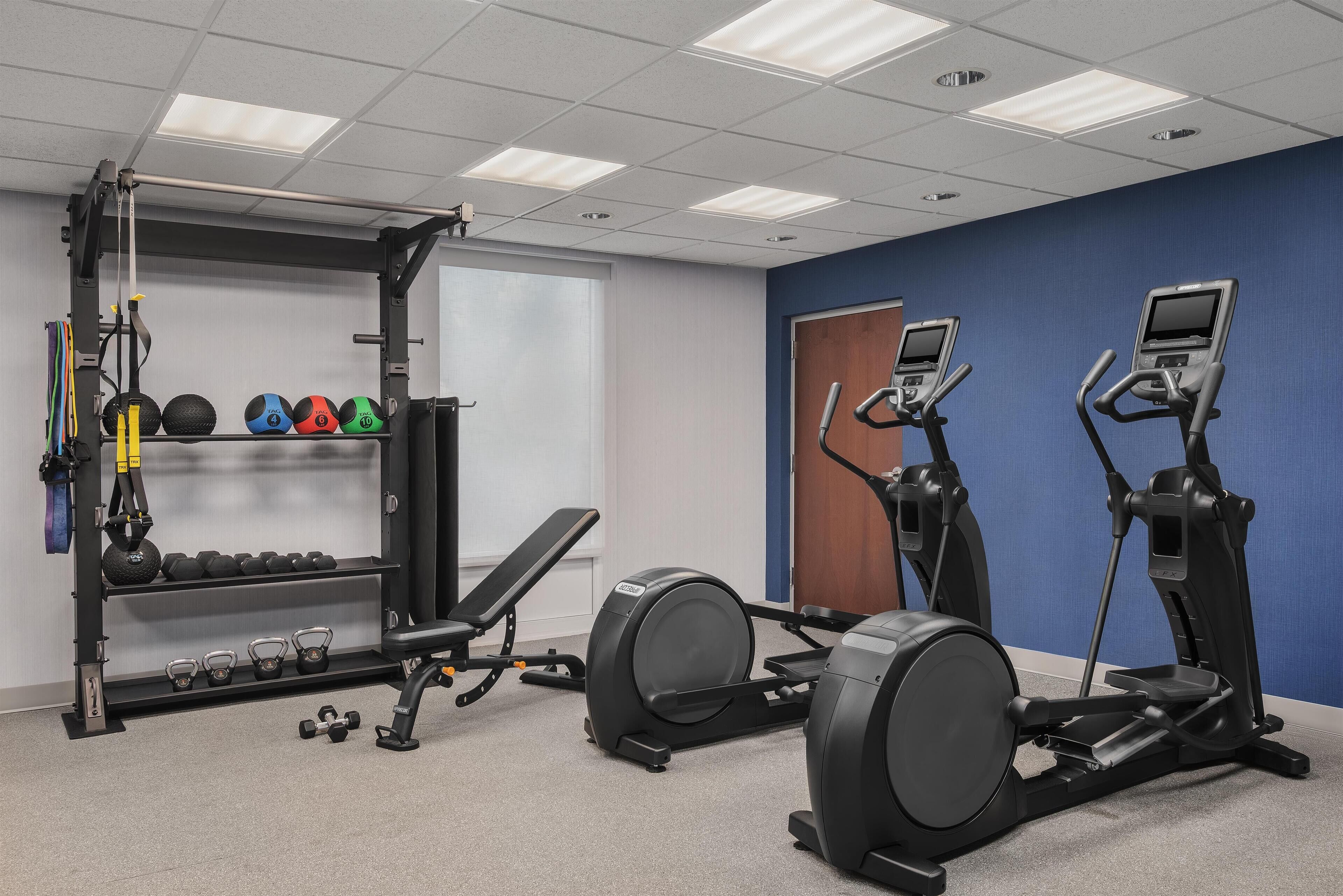 Un gimnasio con equipo de ejercicio, una banca y mancuernas.