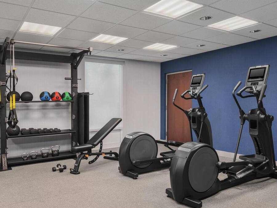 Un gimnasio con equipo de ejercicio, una banca y mancuernas.