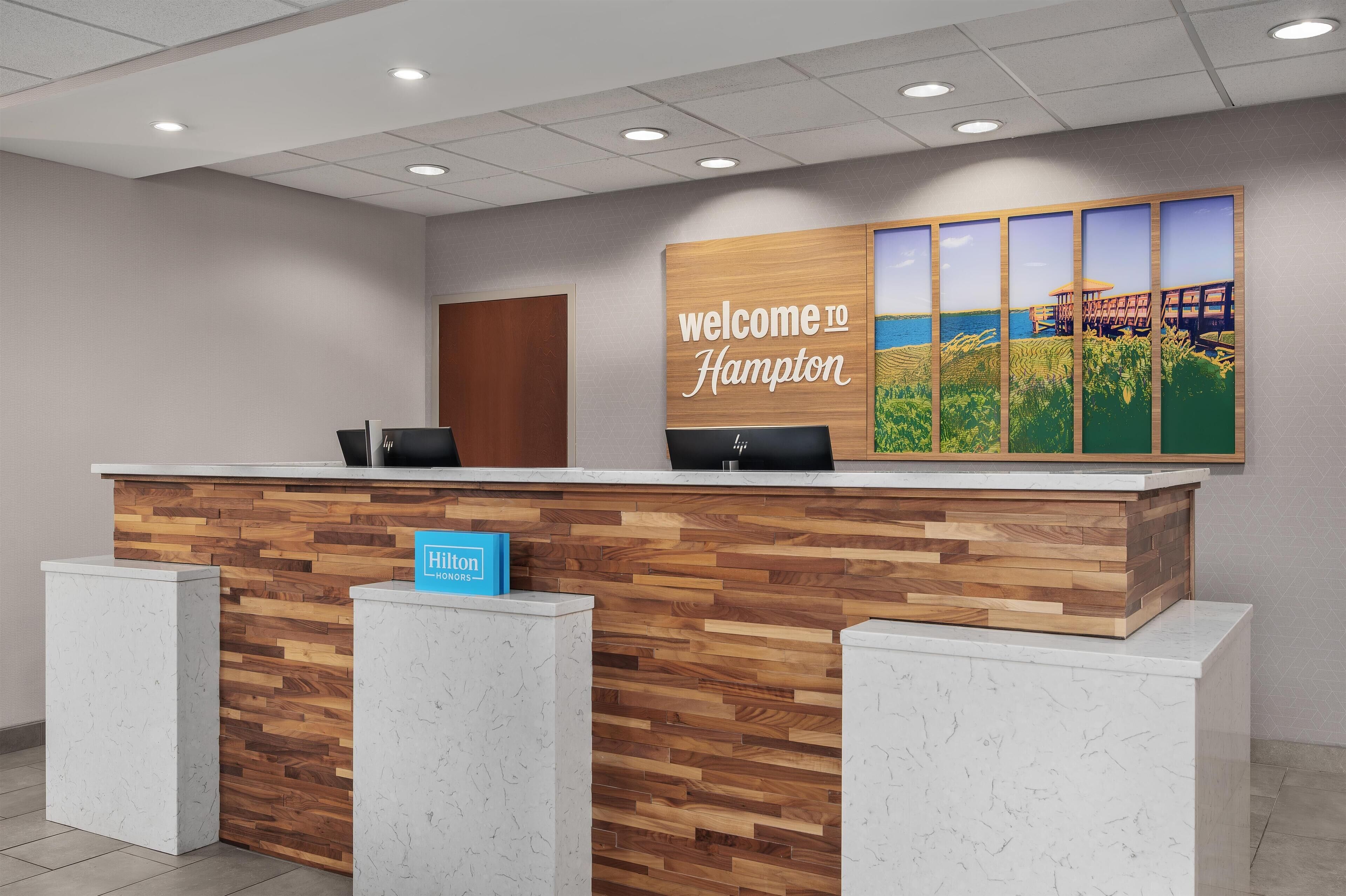 A reception desk with a wooden panel design, a 'Welcome to Hampton' sign, and a 'Hampton' sign on the counter.