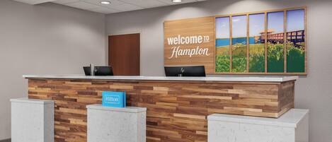 Un mostrador de recepción con detalles de madera, un letrero que dice 'Welcome to Hampton' y un letrero de 'Hampton' en la encimera.