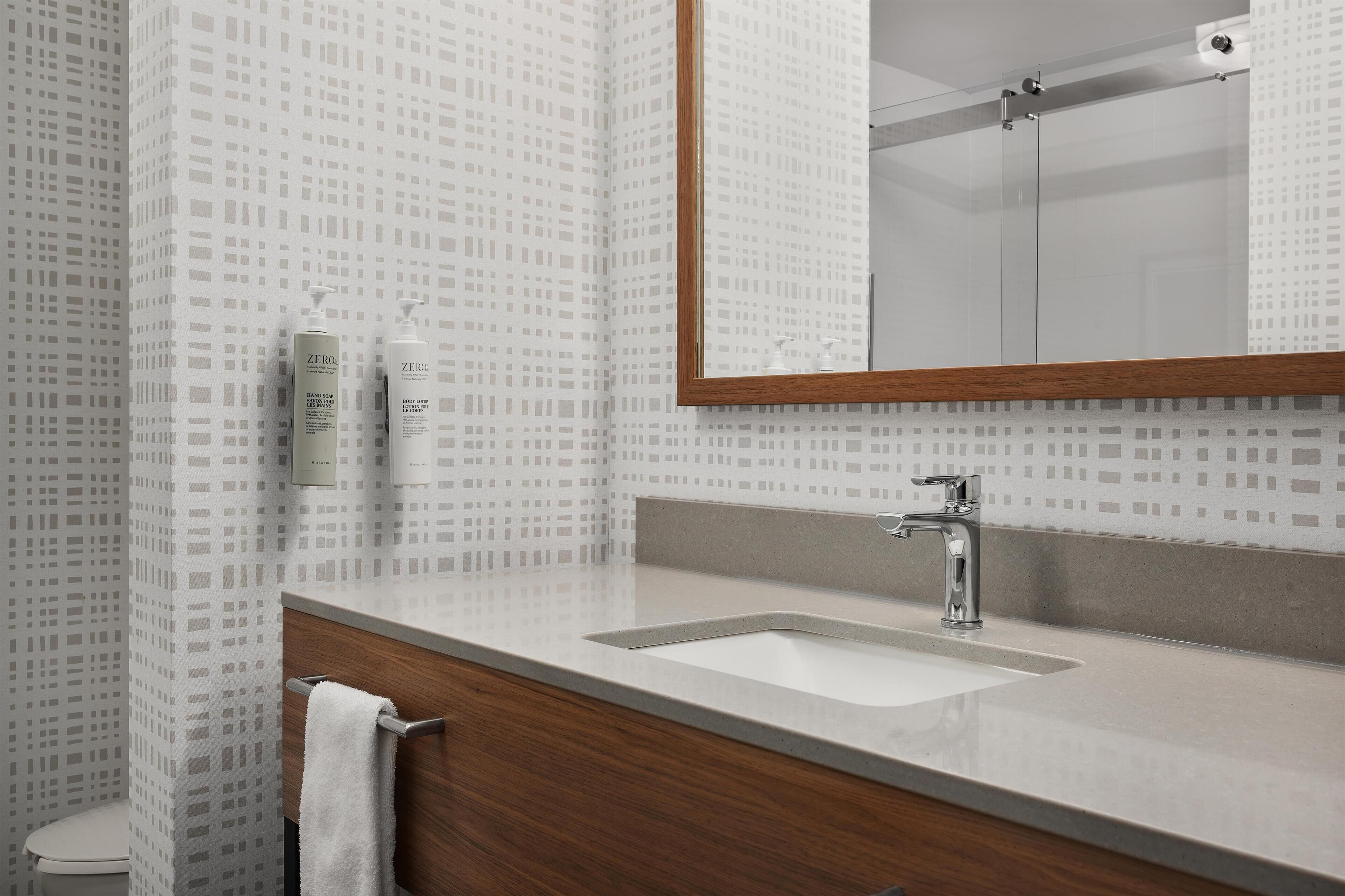 A bathroom with a patterned wall, a wooden vanity, a white sink, and a mirror.