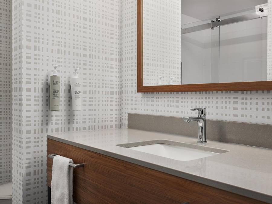 A bathroom with a patterned wall, a wooden vanity, a white sink, and a mirror.
