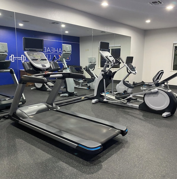 Un gimnasio con cintas de correr, bicicletas estáticas y elípticas.