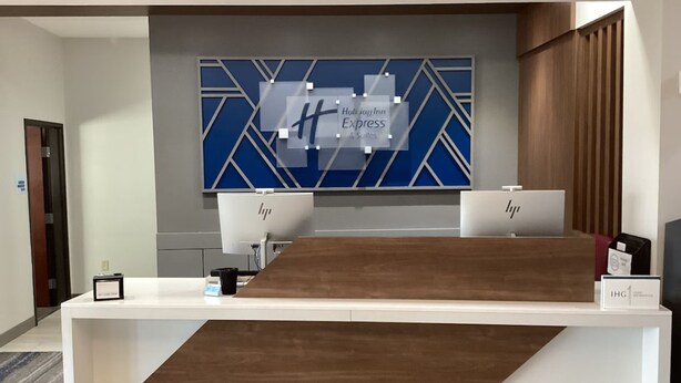 A hotel reception desk with a modern design, featuring a large blue and white geometric wall art, two HP computers, and a sign for Holiday Inn Express & Suites. - Holiday Inn Express &Suites Snyder by IHG (Snyder)