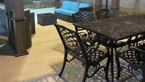 An outdoor patio with a covered seating area, a metal table, and a trash can.