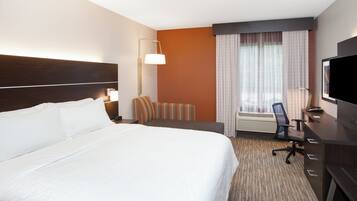 A hotel room with a large bed, a desk with a computer, a TV, and a window with curtains.