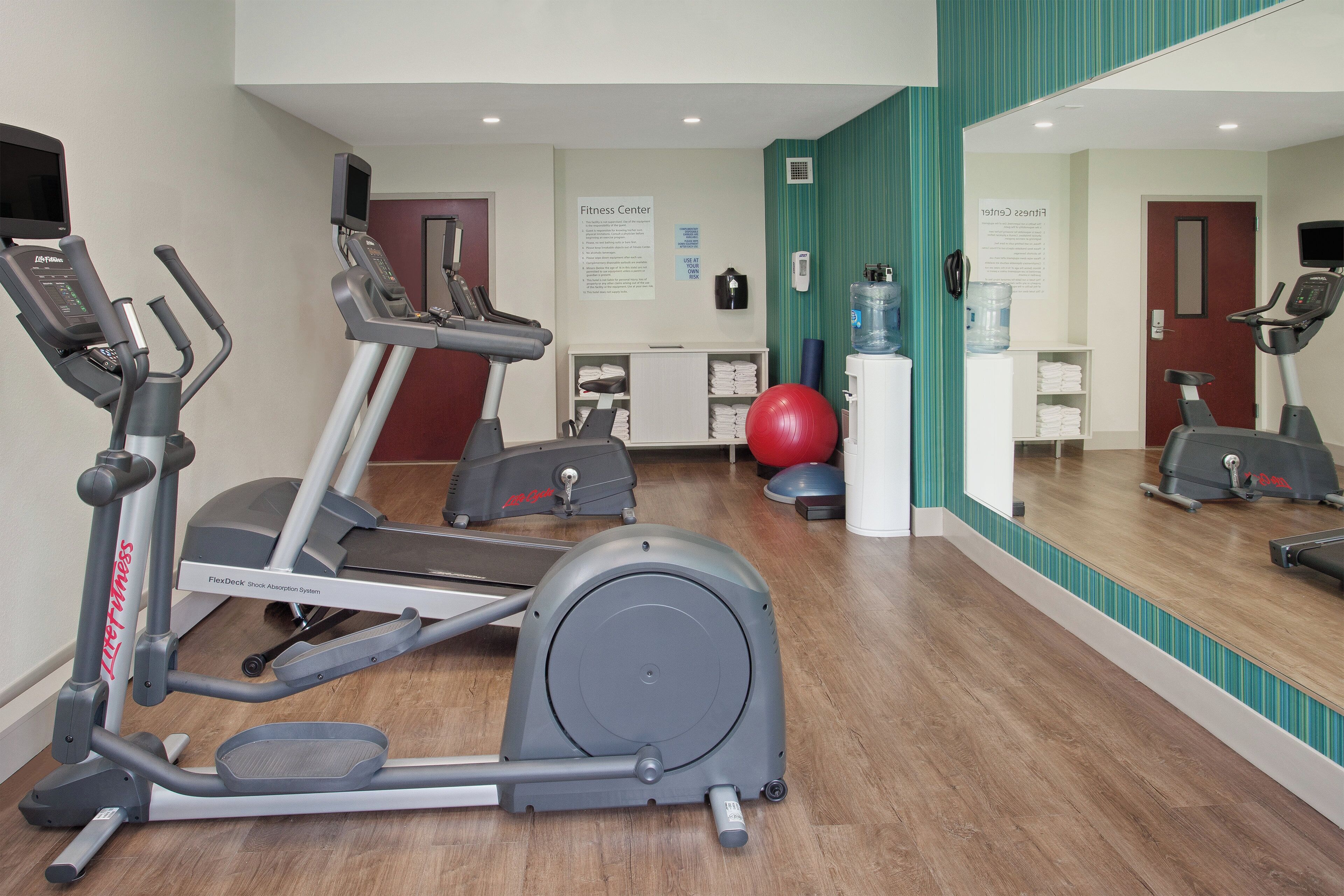 Une salle de sport équipée de tapis de course, d’un vélo d’appartement et d’un ballon d’exercice rouge.