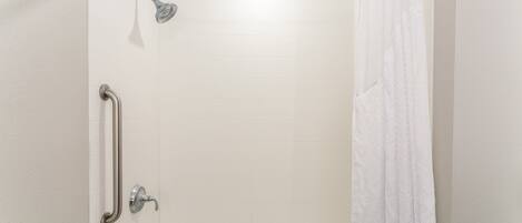 Ein Badezimmer mit weiß gefliesten Wänden, einer Dusche mit Duschbrause, einer Haltestange und einer Badewanne.