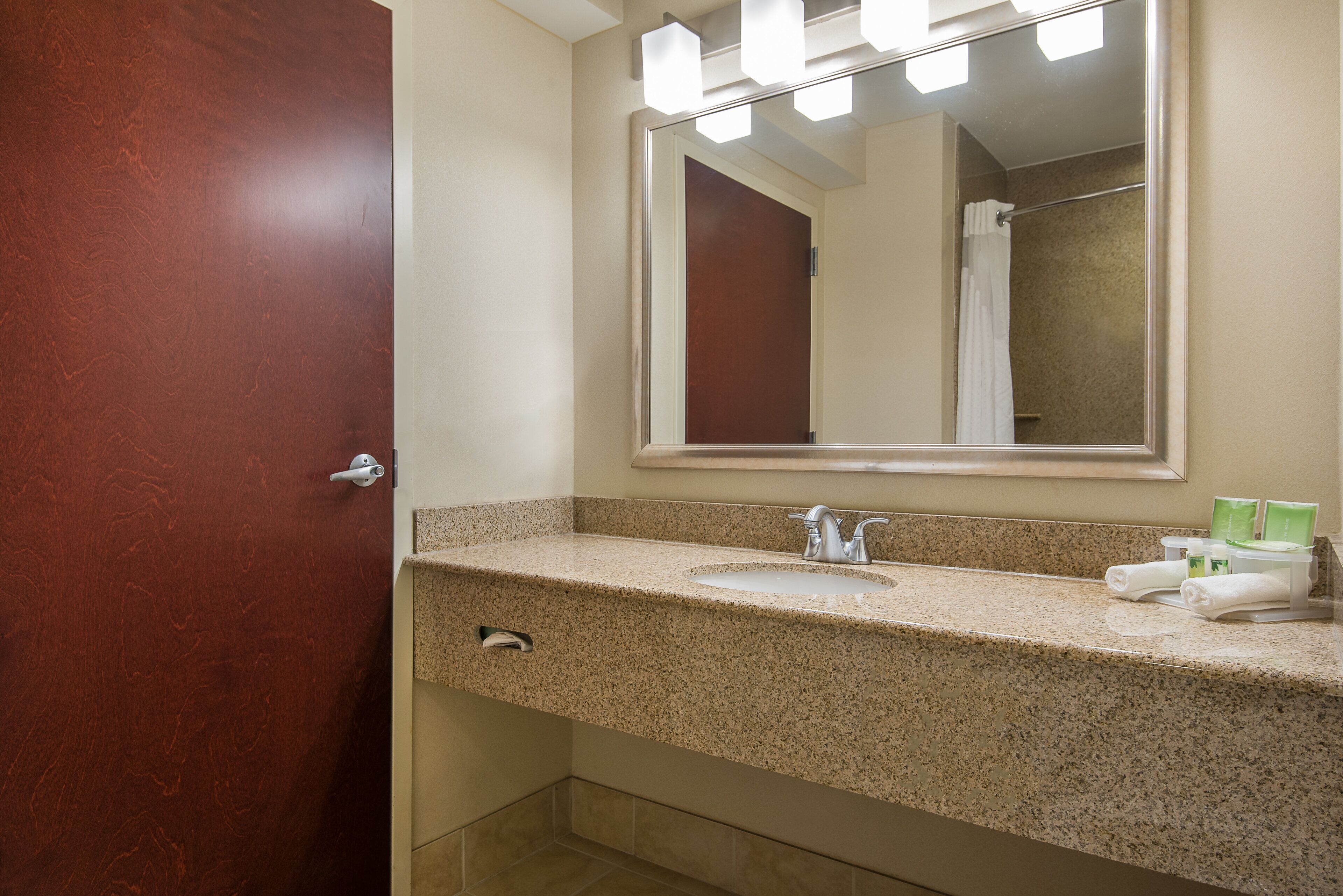A bathroom with a granite countertop, a sink, a mirror, and a shower visible in the reflection.
