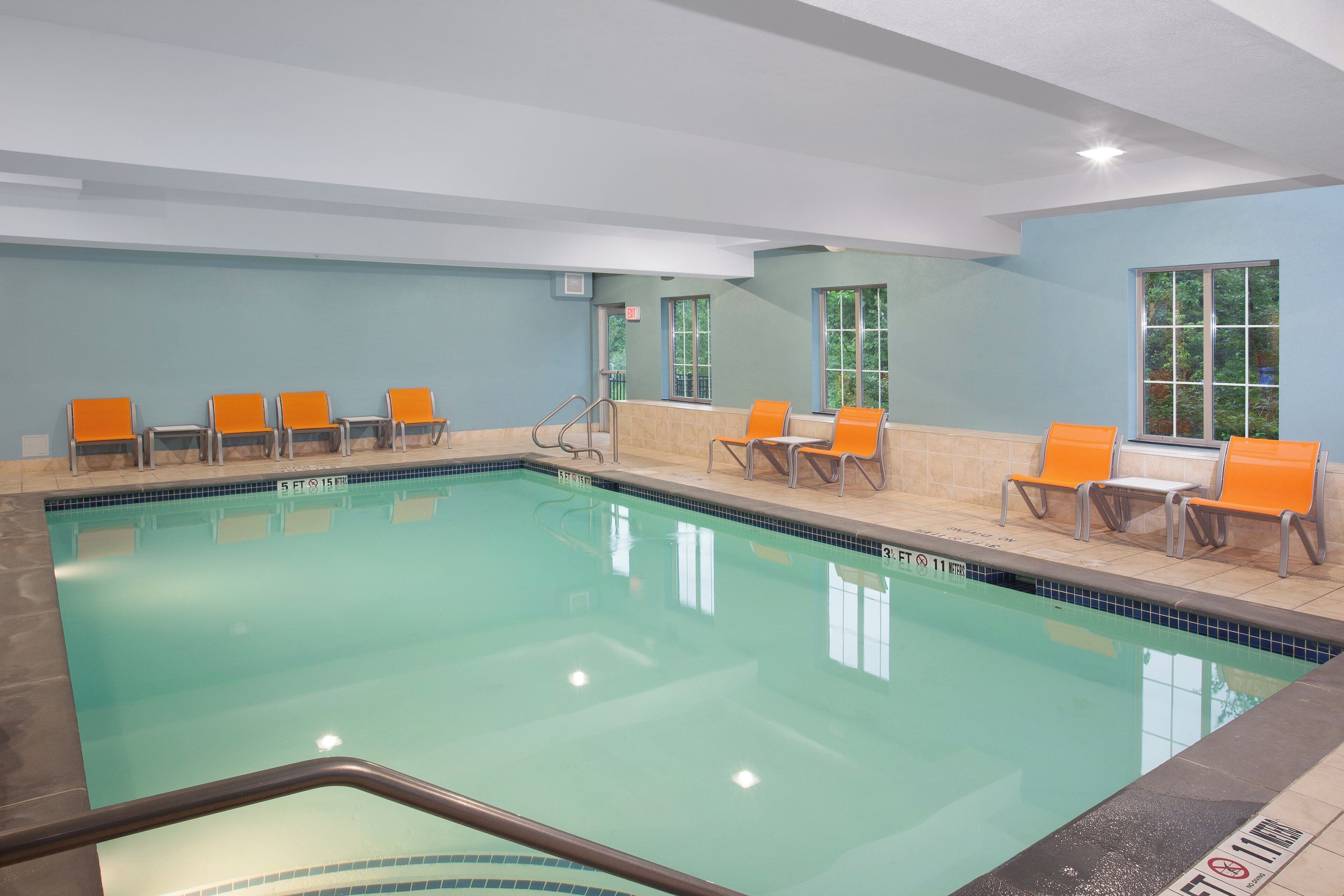 An indoor swimming pool with clear water, surrounded by orange chairs and a tiled floor.