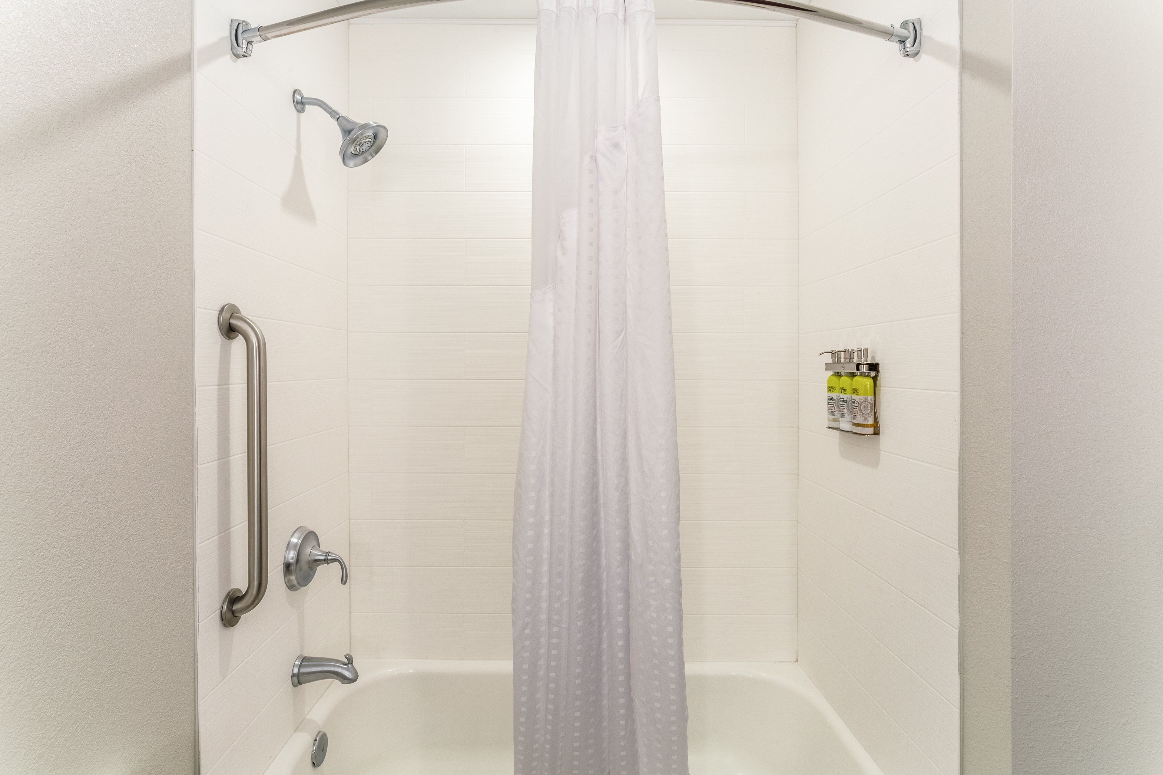 Et bruseområde med badekar, håndbruser, gelænder og en shampoo flaske på væggen.