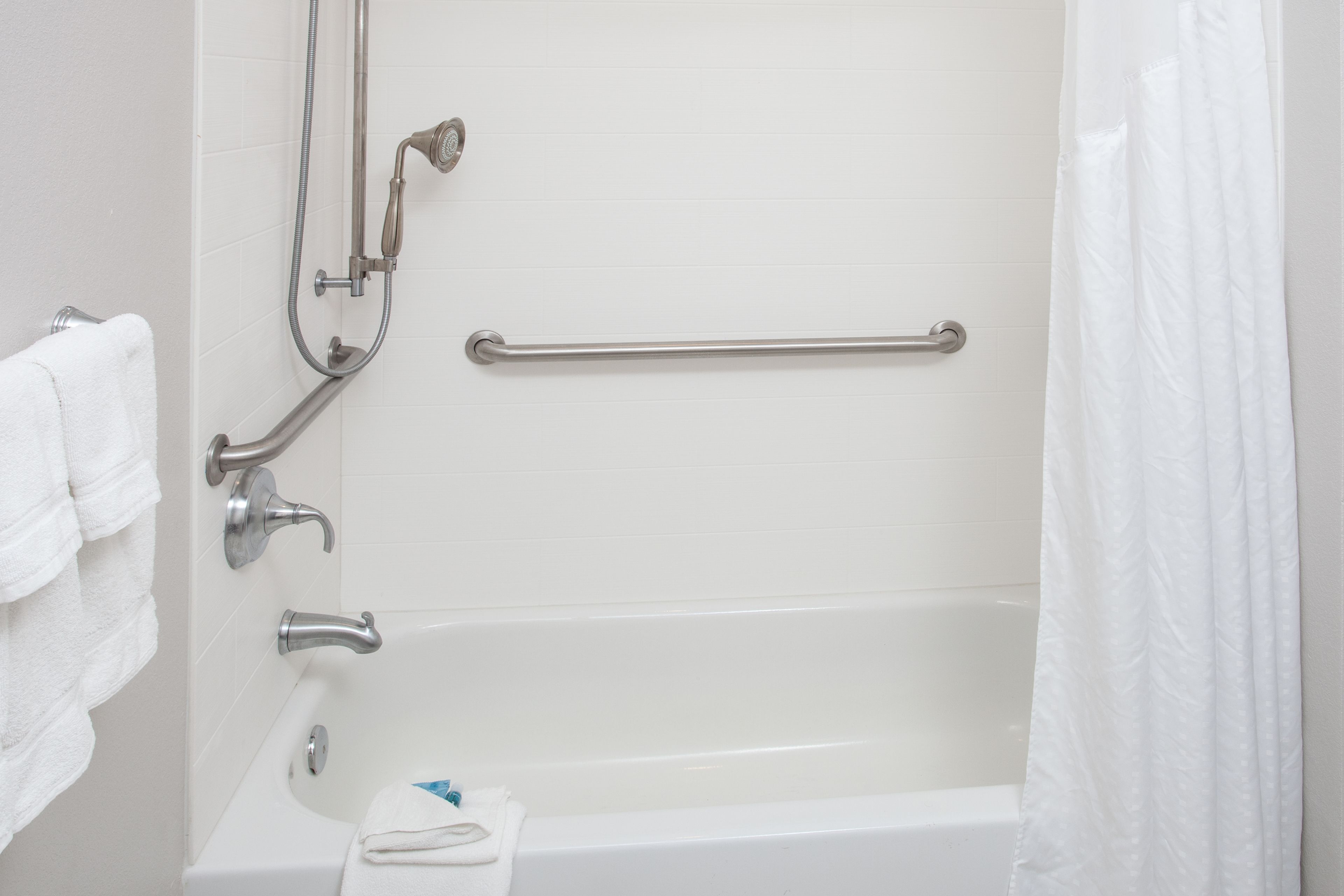Baño con bañera, barras de apoyo y ducha.