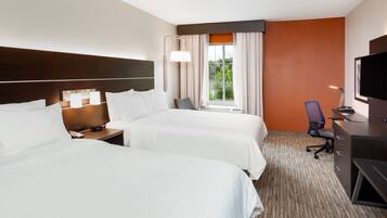 A hotel room with two beds, a desk, a chair, a TV, and a window with curtains.