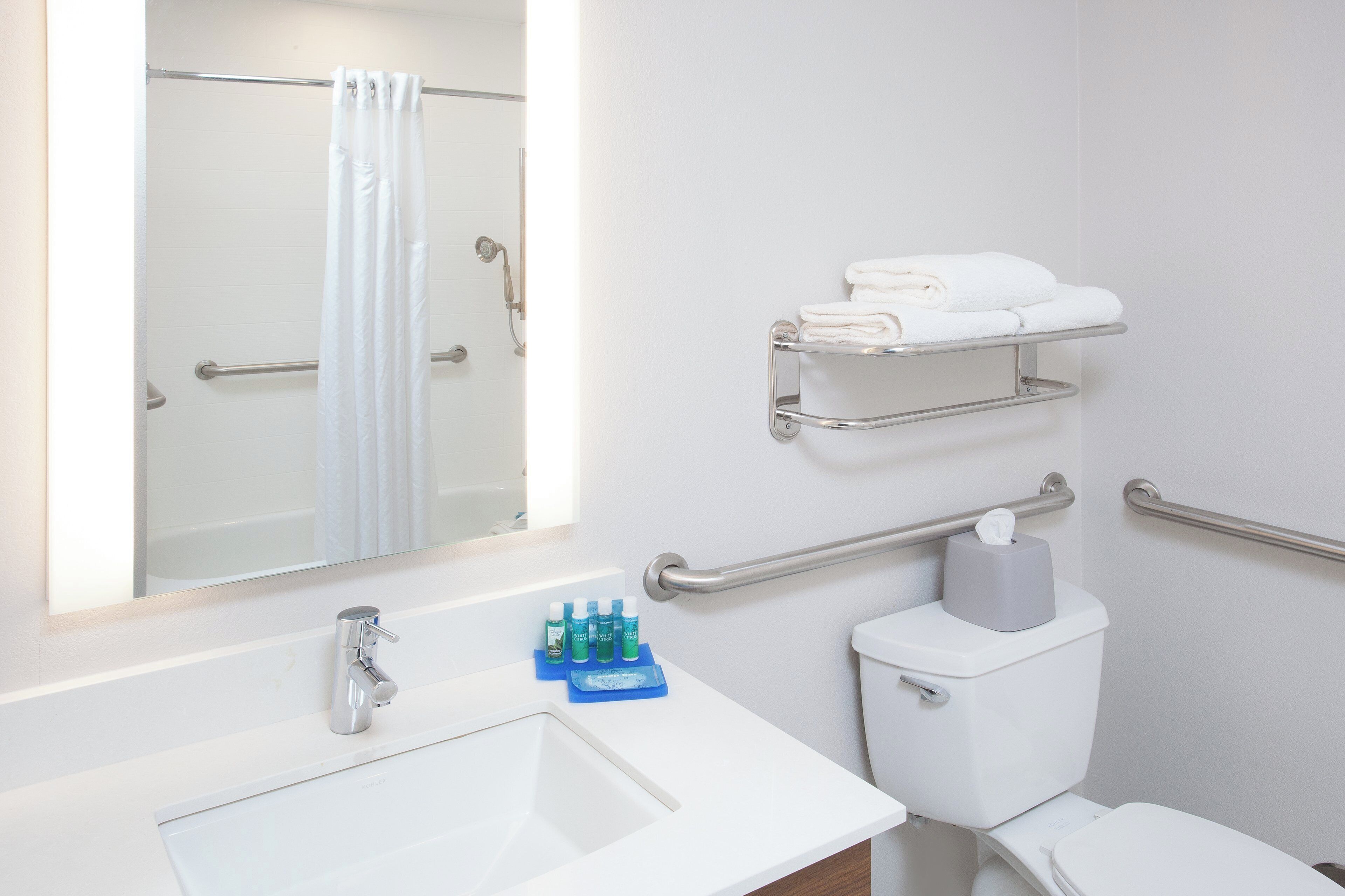 Ein Badezimmer mit weißem Waschbecken, Toilette, Dusche mit weißem Vorhang und Handtuchhalter mit gefalteten Handtüchern.