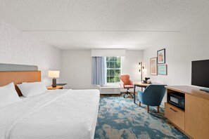 Habitación de hotel con cama, escritorio, silla, televisor y ventana con cortinas.