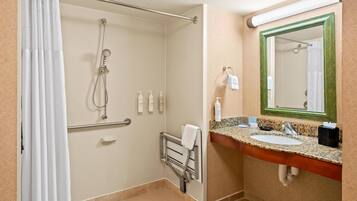 A bathroom with a shower, a handrail, a towel rack, a sink with a mirror, and toiletries.