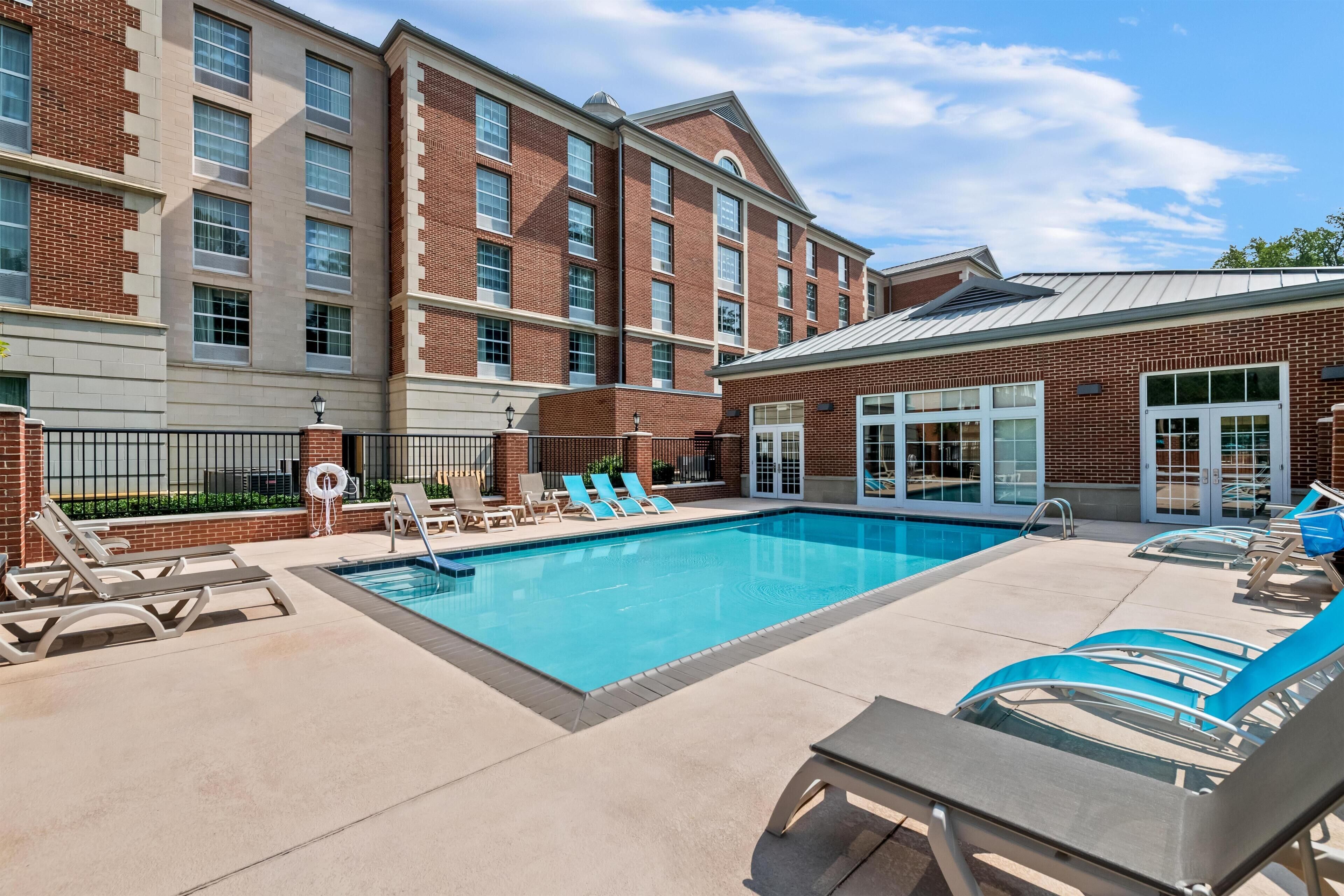 A pool area with lounge chairs and a building with brick facade and large windows.
