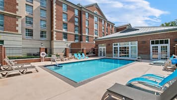 A pool area with lounge chairs and a building with brick facade and large windows.
