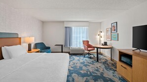 A hotel room with a bed, a desk, a chair, a television, and a window with curtains.