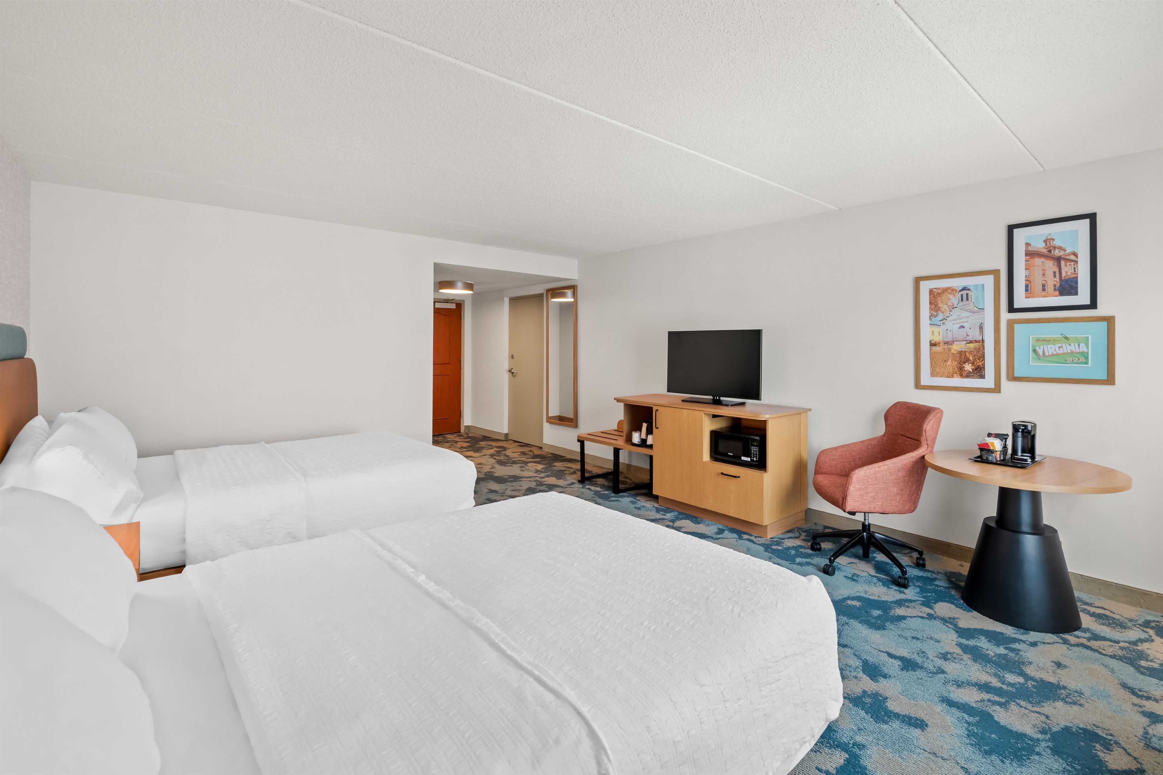 A hotel room with a bed, a desk with a television, a chair, and a small table.