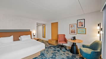 Habitación de hotel con una cama grande, un escritorio con silla, una mesita pequeña y obras de arte colgadas en la pared.