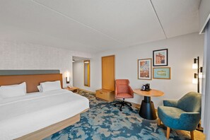 Habitación de hotel con una cama grande, un escritorio con silla, una mesita pequeña y obras de arte colgadas en la pared.