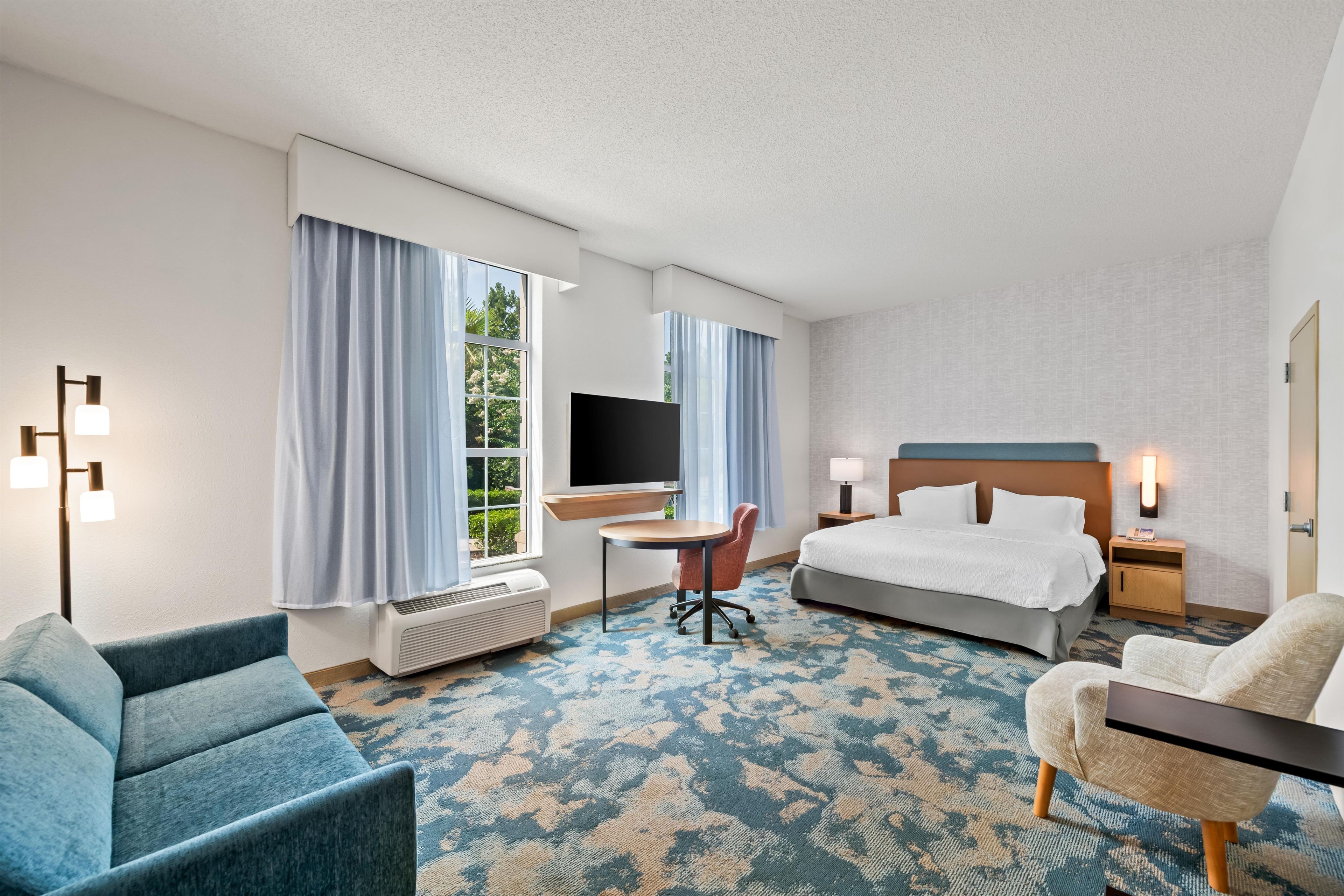 Une chambre d’hôtel avec un lit, un bureau, une chaise, une télévision et une fenêtre avec des rideaux.