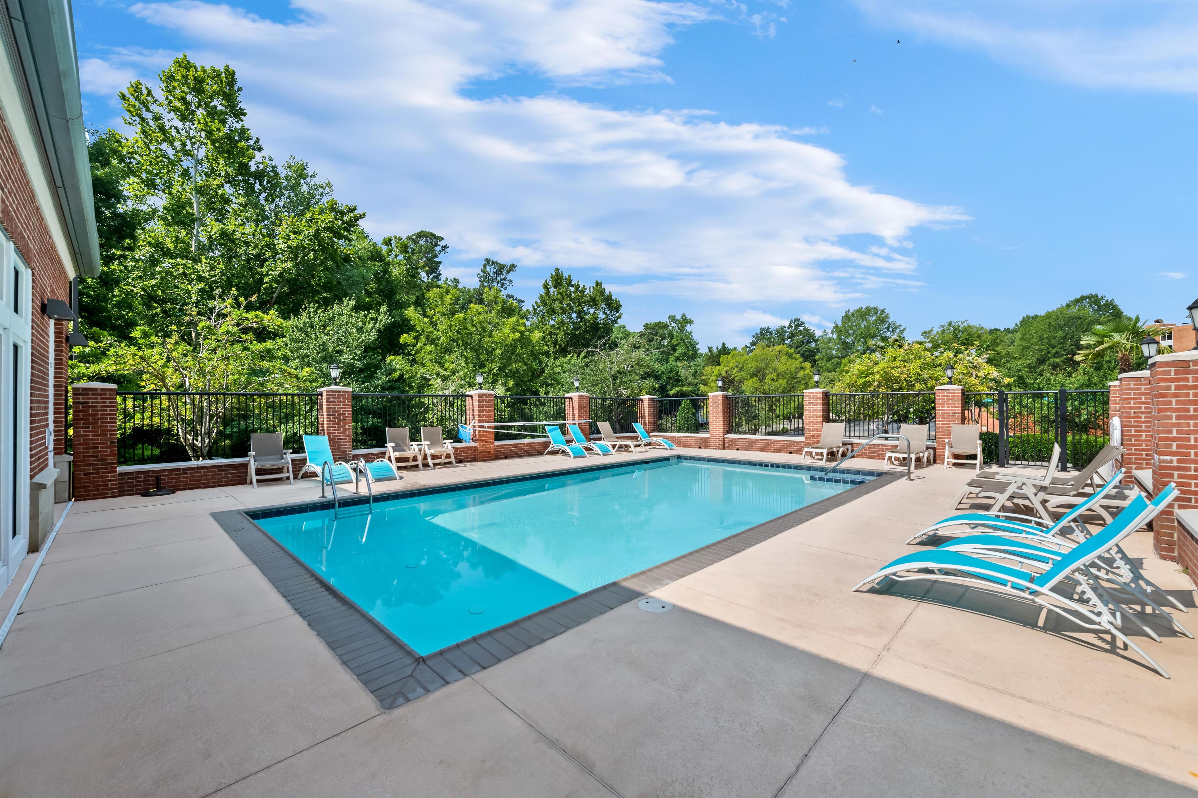 A rectangular outdoor pool with blue water, surrounded by lounge chairs and a brick wall.