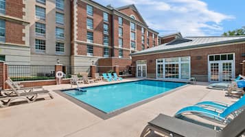 A pool area with lounge chairs and a building with brick facade and large windows.