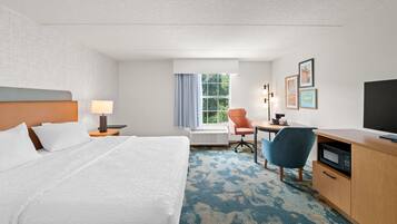 A hotel room with a bed, a desk, a chair, a television, and a window with curtains.