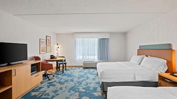 A hotel room with a TV, desk, chairs, a bed, and a window with curtains.