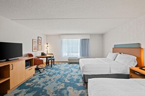 Habitación de hotel con televisión, escritorio, sillas, cama y ventana con cortinas.