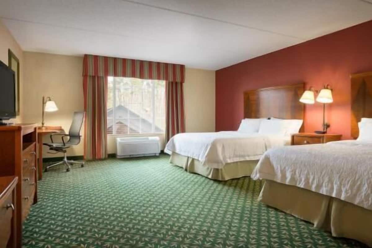 A hotel room with two beds, a desk, a chair, a television, and a window with curtains.
