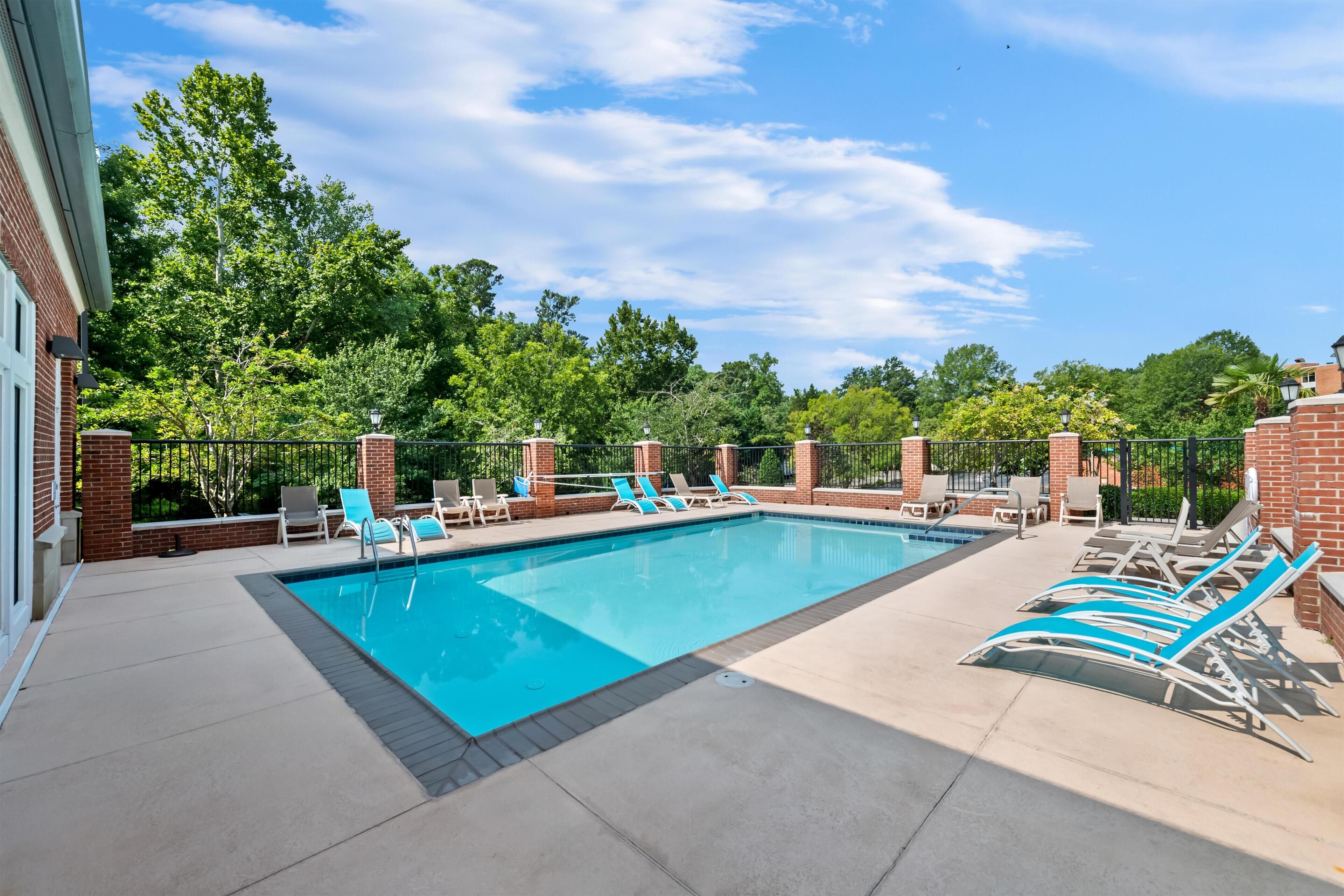 A rectangular outdoor pool with blue water, surrounded by lounge chairs and a brick wall.