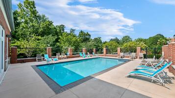 A rectangular outdoor pool with blue water, surrounded by lounge chairs and a brick wall.