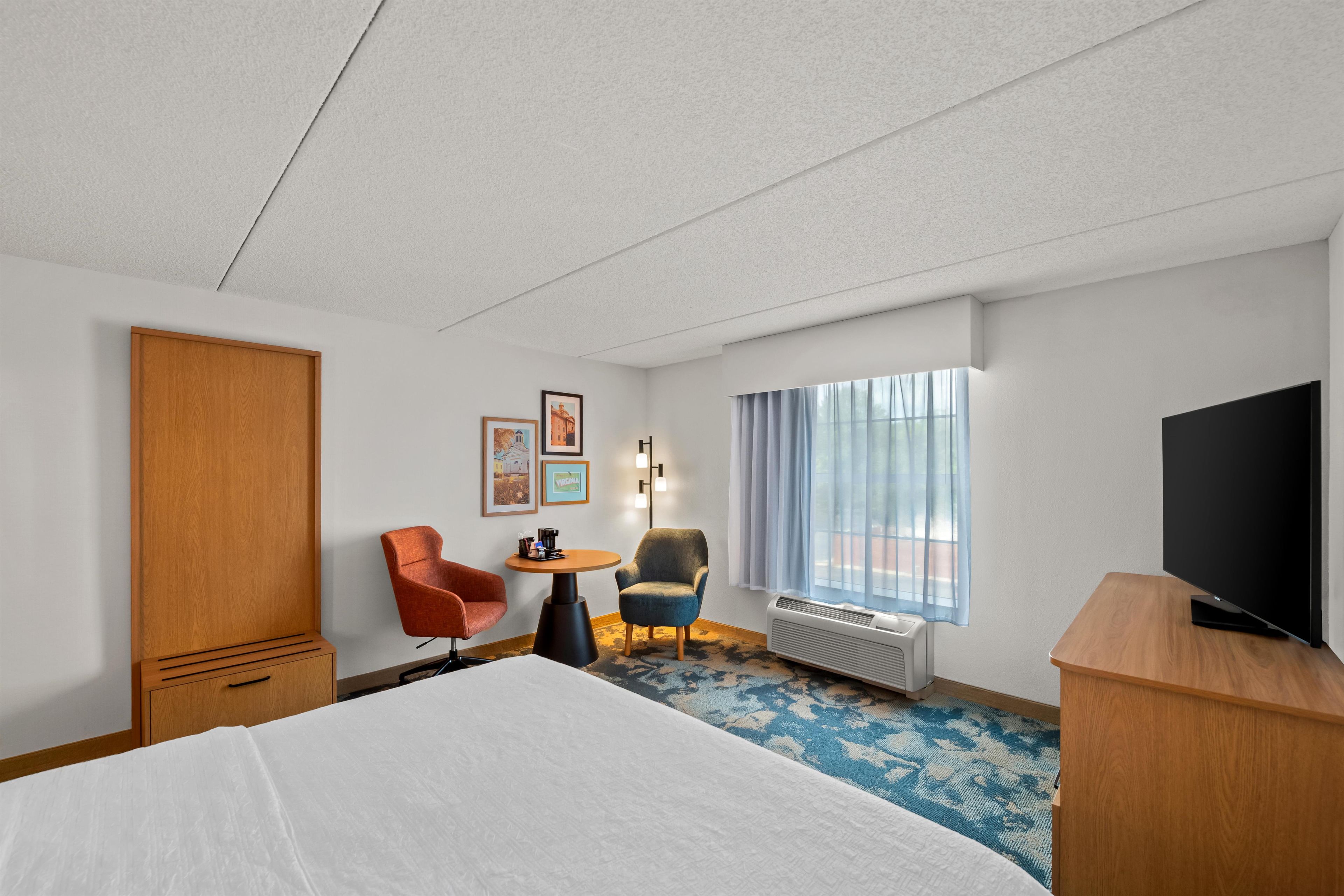 Ein Hotelzimmer mit einem Bett, einem Fernseher, einem Schreibtisch mit Stuhl und einem Fenster mit Vorhängen.