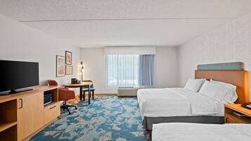 A hotel room with a TV, desk, chairs, a bed, and a window with curtains.