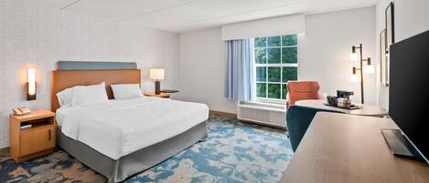 Quarto de hotel com cama, mesas de cabeceira, escrivaninha, cadeira, televisão e janela com cortinas.