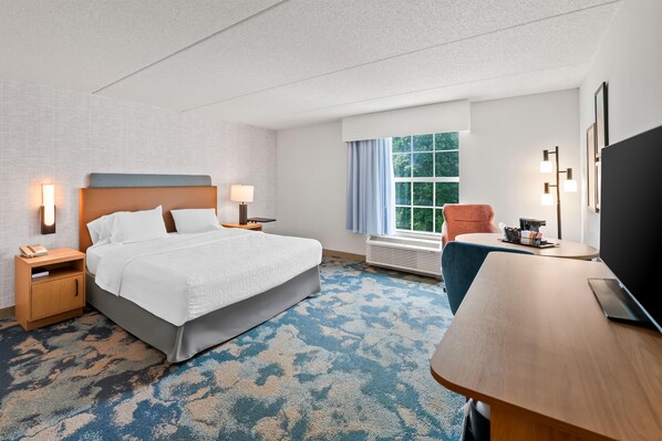 A hotel room with a bed, bedside tables, a desk, a chair, a TV, and a window with curtains.