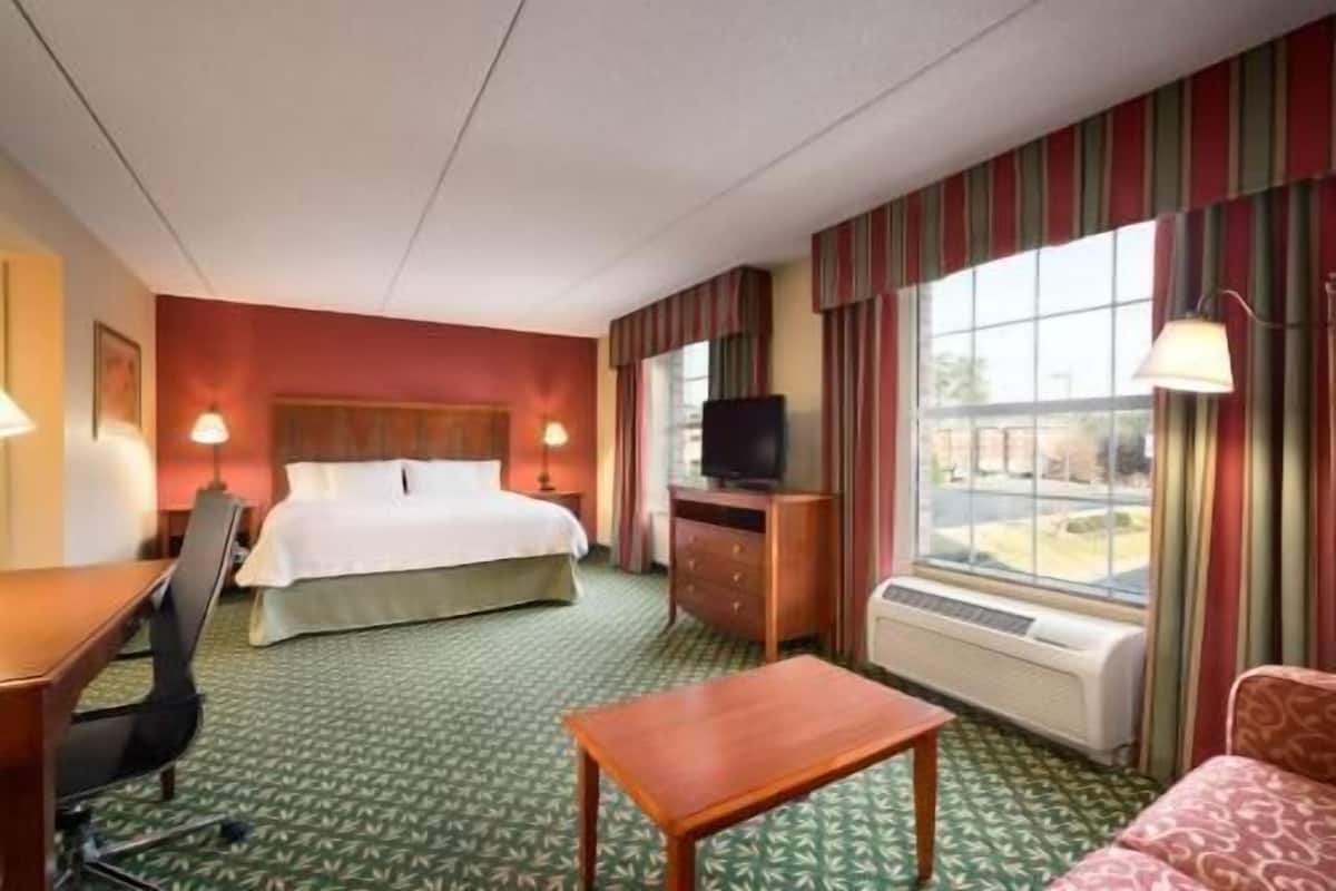A hotel room with a bed, a desk, a television, a window with curtains, and a patterned carpet.