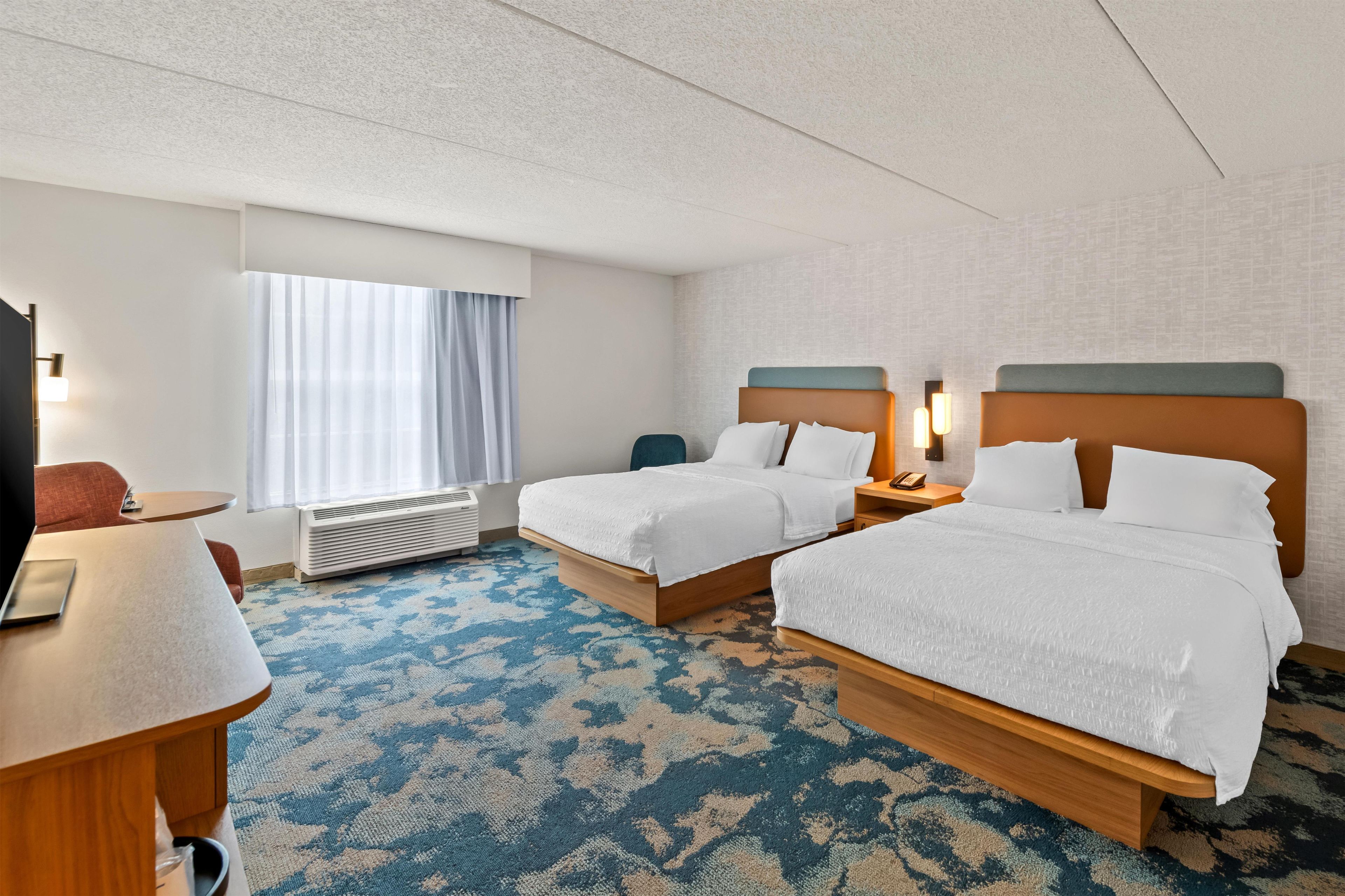 A hotel room with two beds, a desk, a chair, a TV, and a window with curtains.