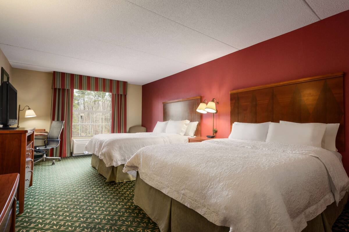 A hotel room with two beds, a desk, a chair, and a TV.