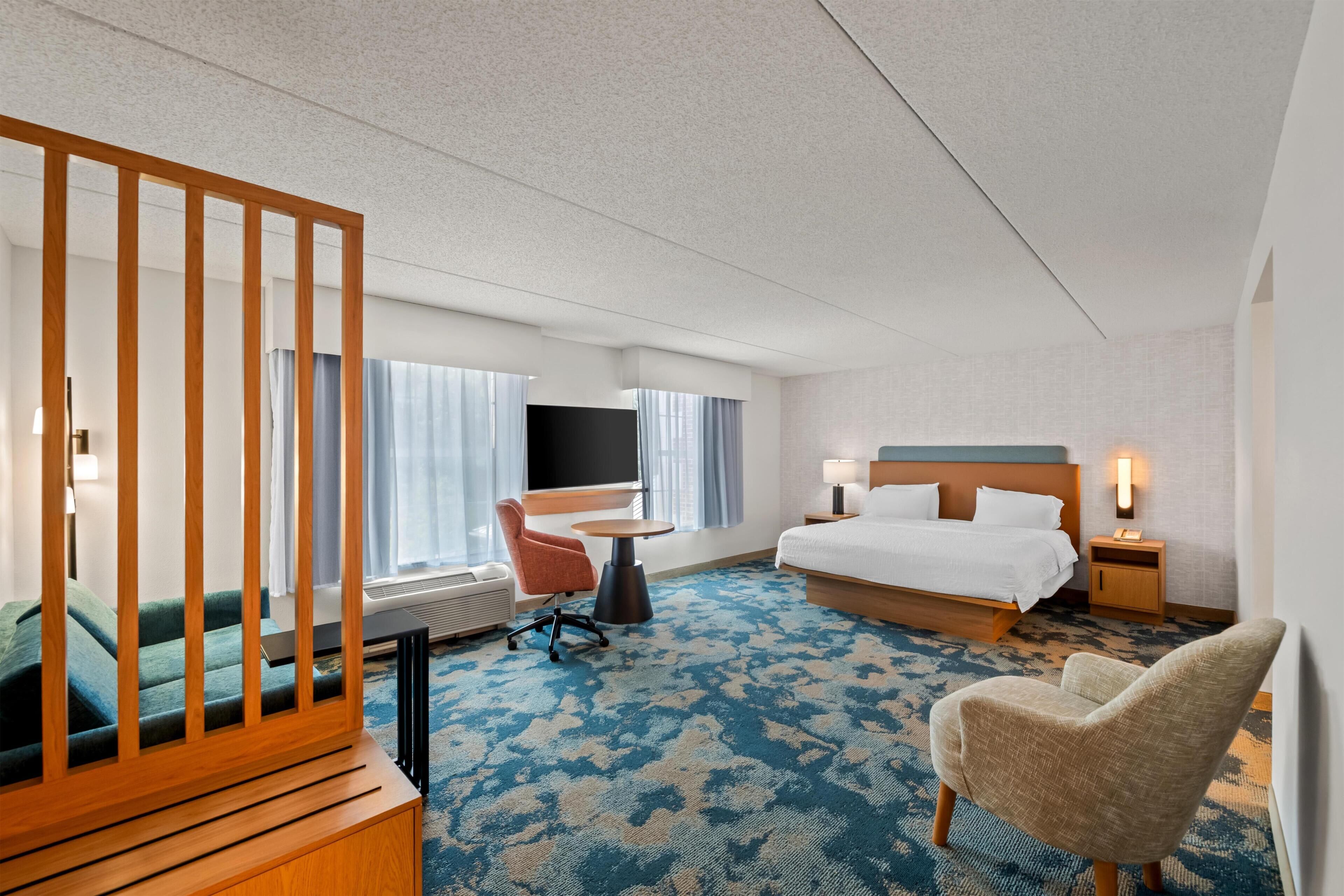 A hotel room with a bed, a desk, a chair, a TV, and a window with curtains.