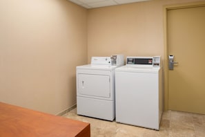 A laundry room with two stacked washers and dryers, a wooden table, and a door. - Hampton Inn & Suites Williamsburg-Central (Williamsburg)