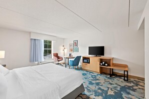 A hotel room with a bed, a desk with a TV, a chair, a small table, and a window with curtains. - Hampton Inn & Suites Williamsburg-Central (Williamsburg)