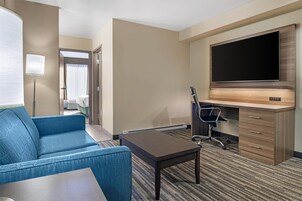 Habitación de hotel con sofá azul, un escritorio con silla, televisor de pantalla plana montado en la pared y una lámpara.