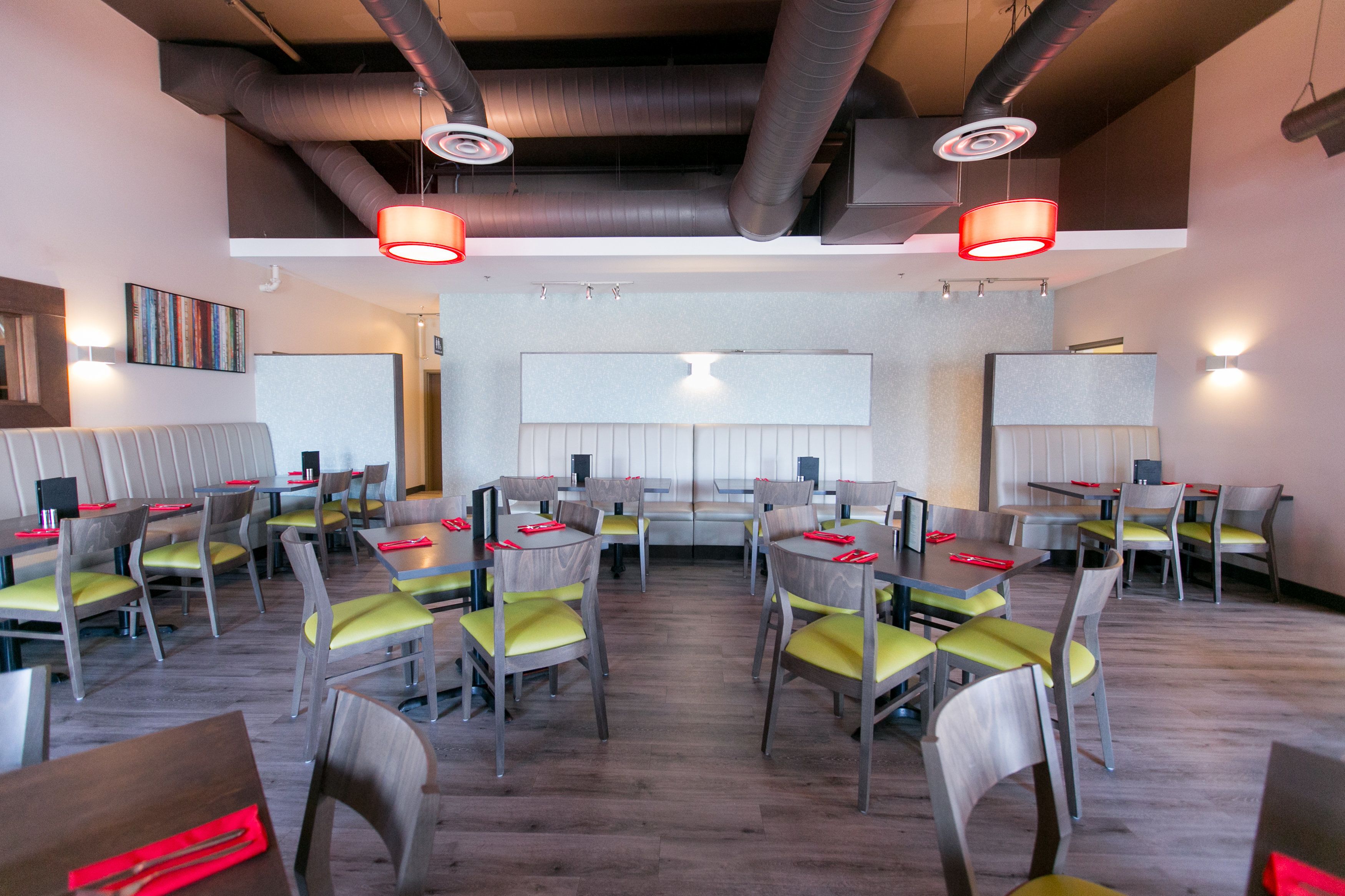 Ein Restaurant mit mehreren Tischen und Stühlen, einer hohen Decke mit freiliegenden Lüftungsrohren und einer neutralen Farbgestaltung.